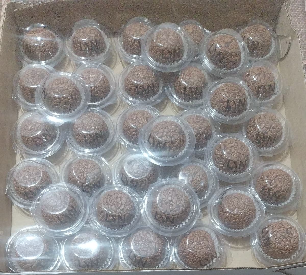 Caixa com dezenas de brigadeiros em cápsulas plásticas, cada um com o logo Lynk Markets aplicado.