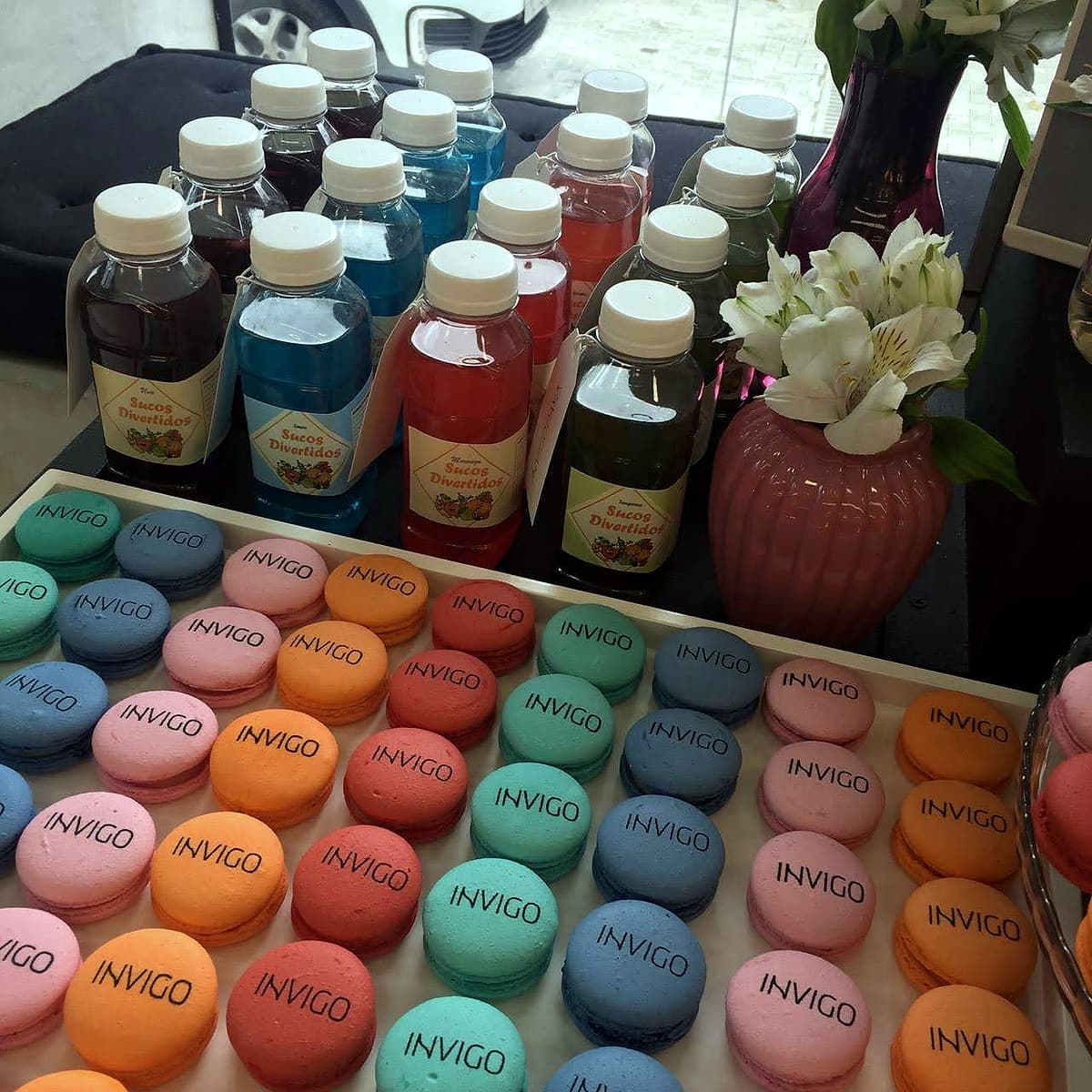 Close de bandeja com macarons nas cores laranja, rosa, azul e verde, todos carimbados com a palavra INVIGO.