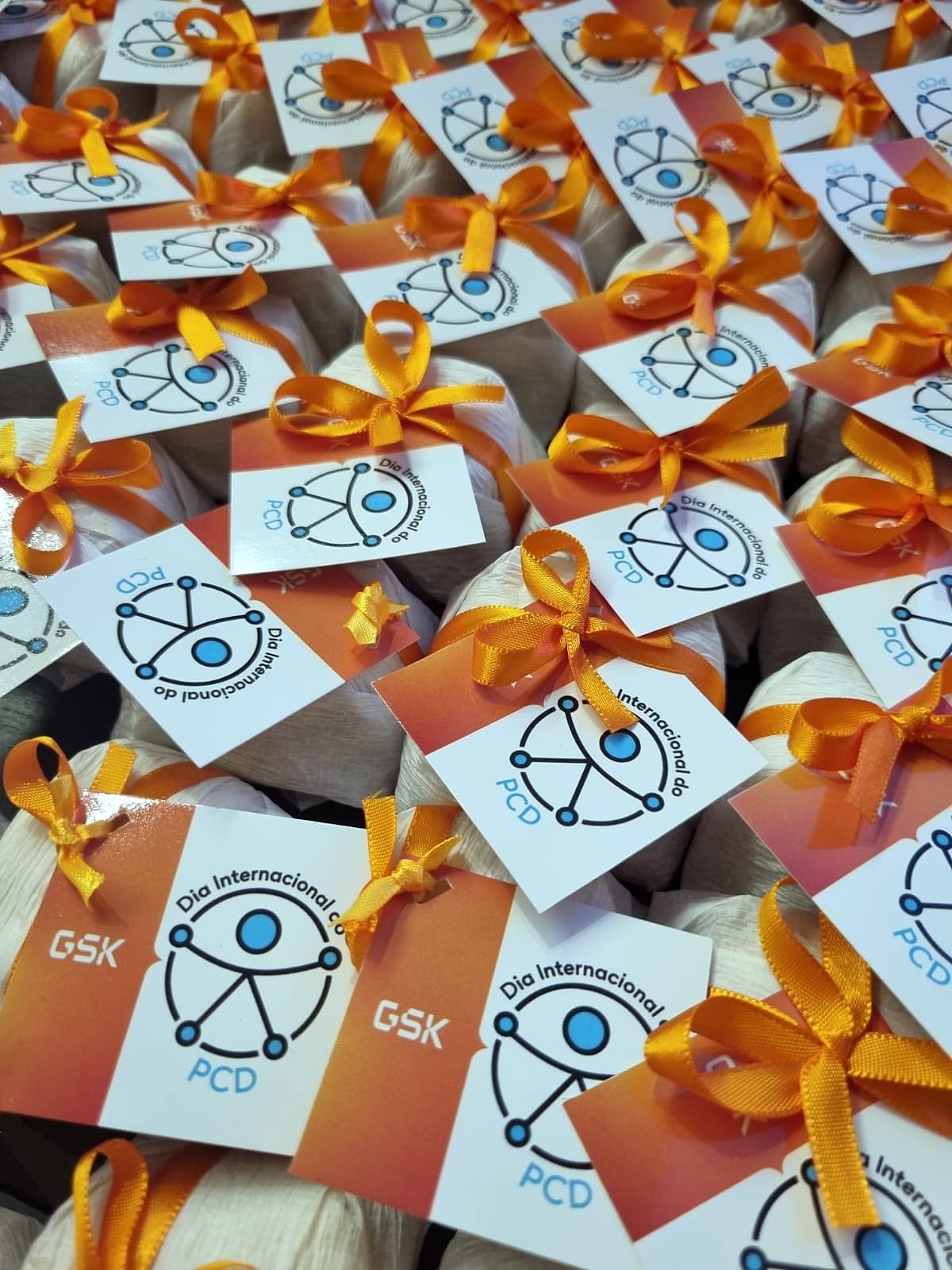 Dezenas de lembranças embaladas com laço laranja e tag do Dia Internacional da PCD com logo GSK.
