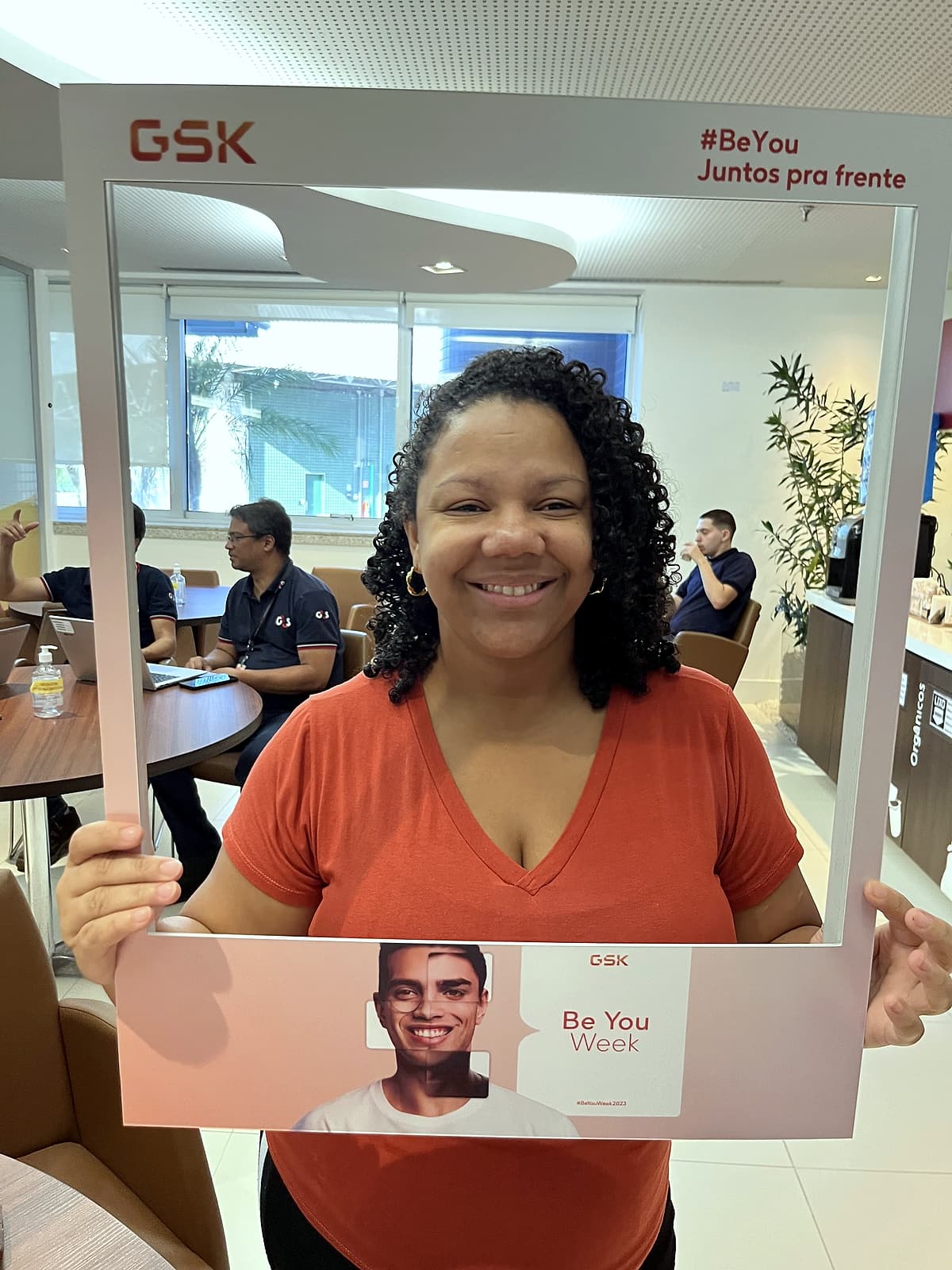 Colaboradora sorrindo segurando moldura de foto GSK '#BeYou Juntos pra frente – Be You Week'.