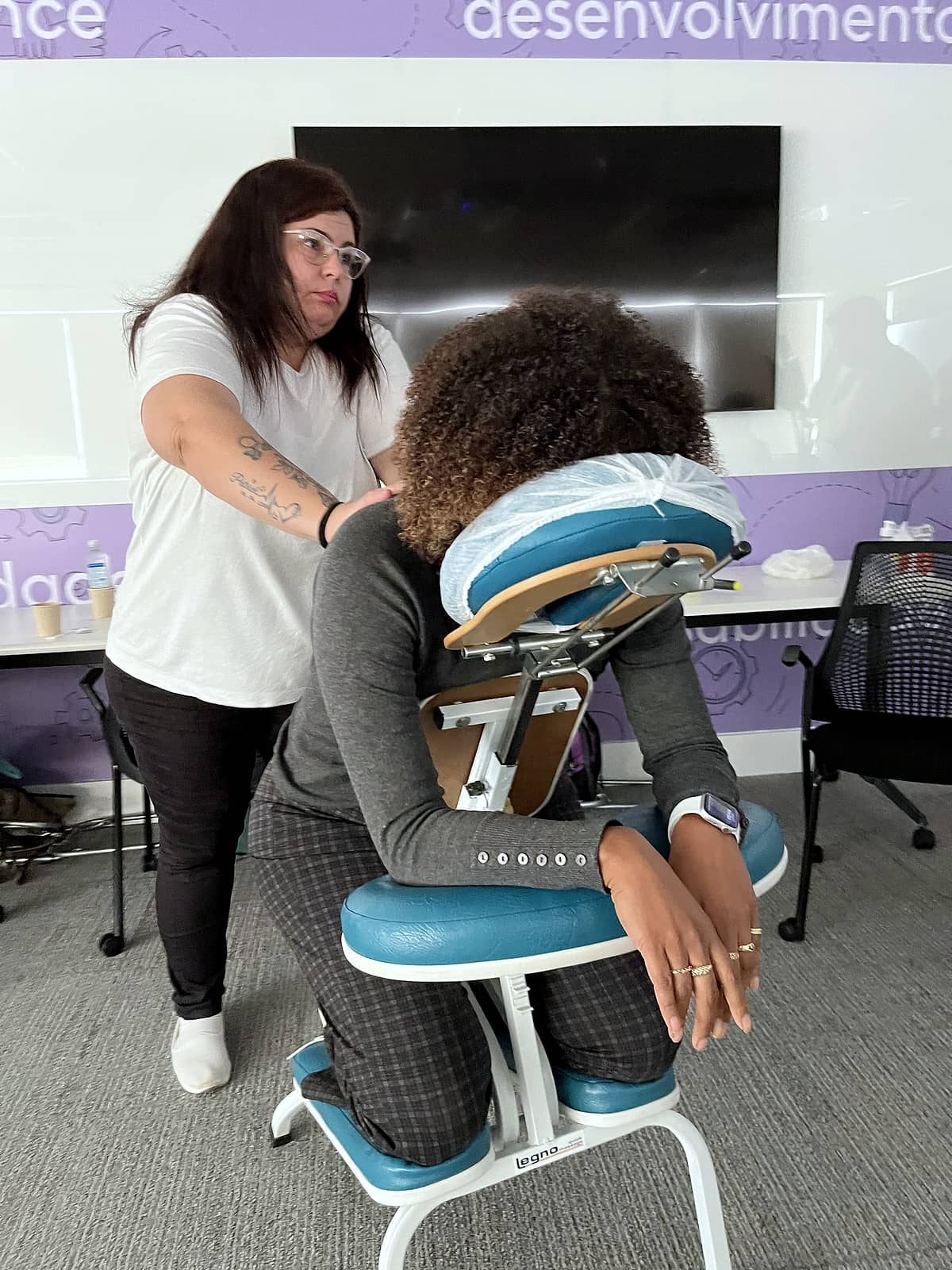 Massoterapeuta aplica quick massage em colaboradora sentada em cadeira ergonômica de massagem.