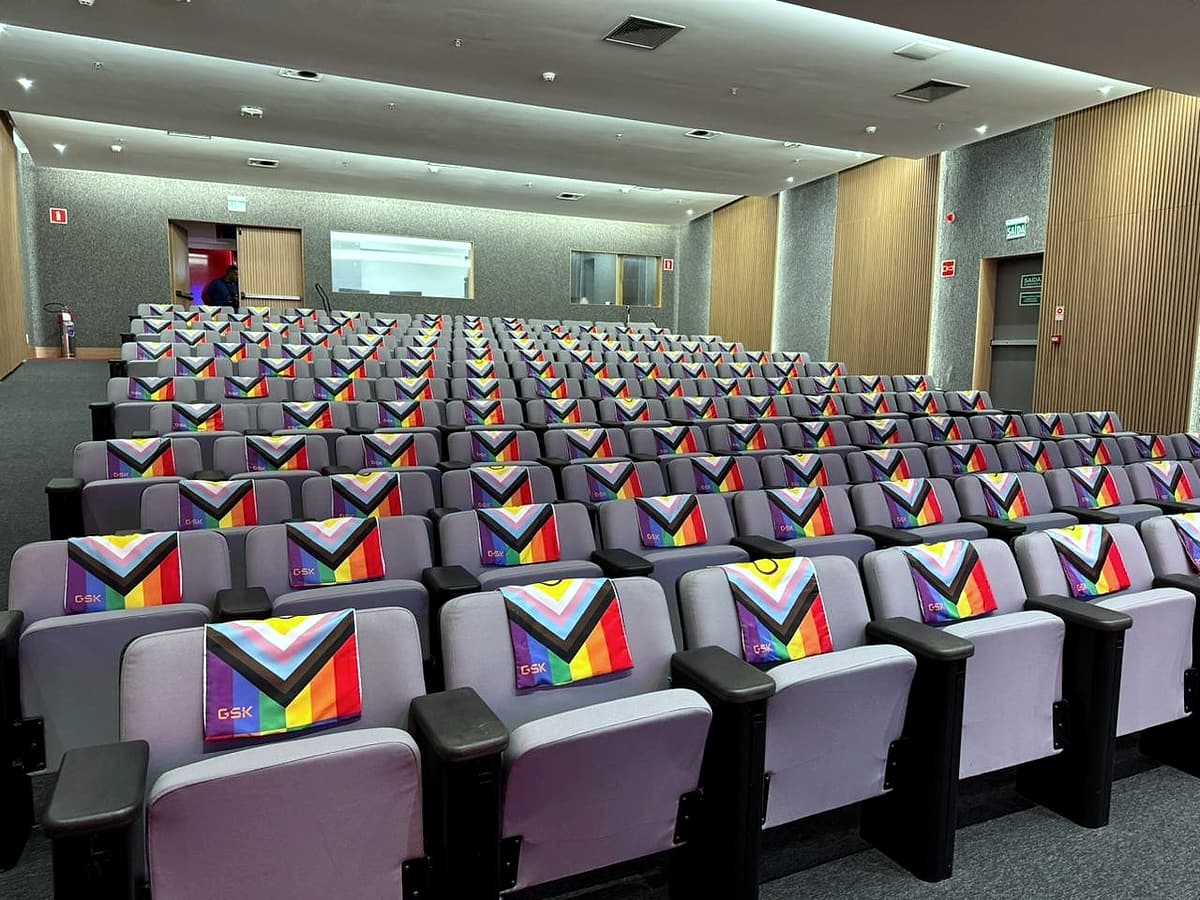 Auditório com fileiras de poltronas lilás, cada uma com capa estampada com a bandeira do Orgulho no formato Progress.