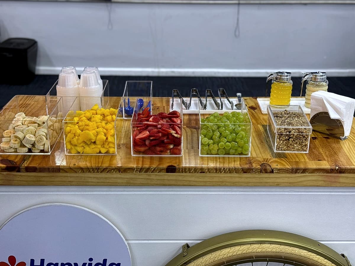 Cubas de acrílico com banana, manga, morango, uva e granola sobre tampo de madeira.