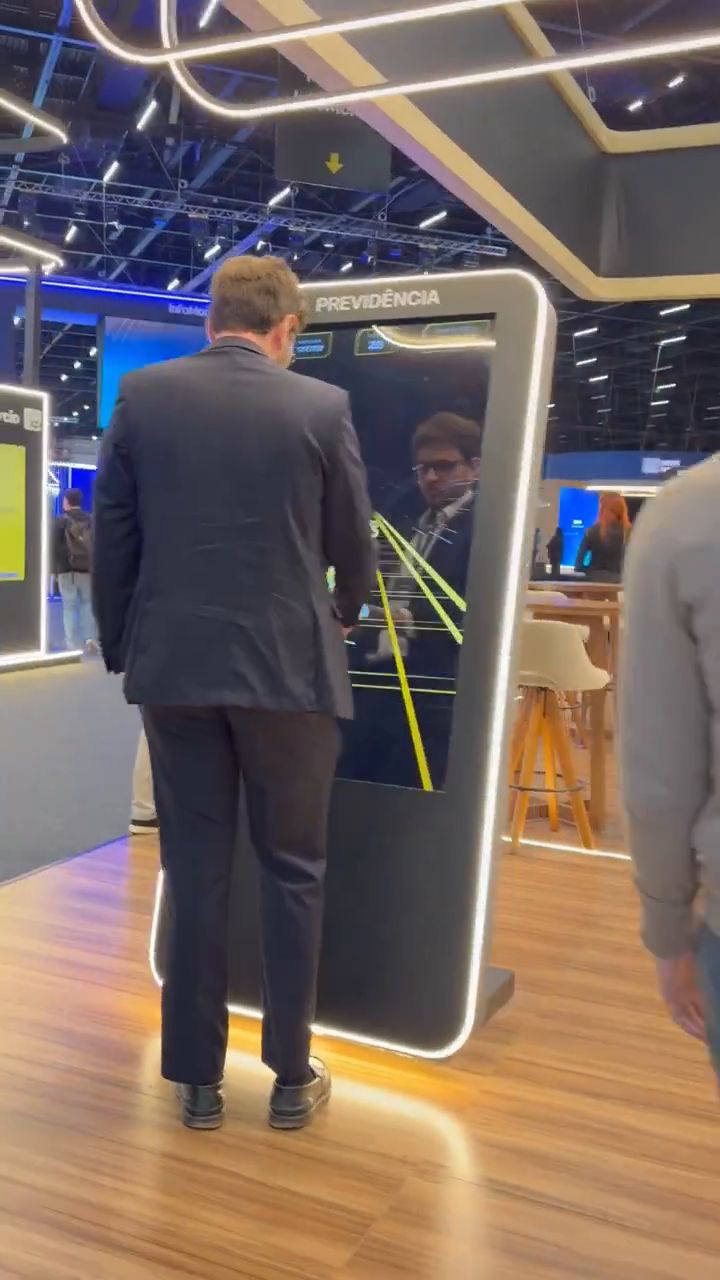 Um participante de terno joga Acelerador do Futuro em frente a um totem vertical iluminado da XP Previdência.